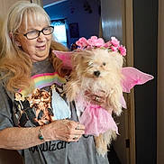 Nana is registered to the contest to win money with this photo: bracelet, costume, curtain, dog, doorway, fairy_wings, flower_crown, glasses, gray_shirt, happy, holding, indoor, light, long_hair, pet, pink, rings, smile, window, woman