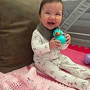 Addison joined the competition — help win amazing prizes! baby, child, smiling, toy, rubber_duck, pink_blanket, floral_onesie, pillow, playpen, indoor, cute, happy, sitting, infant, face, hand, clothing, head, person, portrait