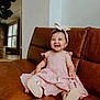 baby, child, smiling, pink_dress, headband, bow, leather_couch, indoor, living_room, mirror, plant, happy, sitting, footwear, modern, natural_light, portrait, cute, infant, home_decor
