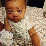 Kimani joined the competition — help win amazing prizes! baby, child, pajamas, animal_print, bed, plaid, hand, skin, face, eyes, infant, cute, indoor, person, clothing, sleepwear, young, expression, sitting, portrait