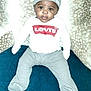 Kimani joined the competition — help win amazing prizes! baby, child, infant, hat, clothing, shirt, pants, footed_pants, sitting, blue_surface, patterned_background, indoor, person, face, eyes, expression, levis_logo, headwear, cute, young_child