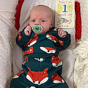 Oakley joined the competition — help win amazing prizes! baby, infant, pacifier, fox_pattern, blanket, milestone_card, cozy, cute, newborn, clothing, lying_down, white, red, green, soft_texture, portrait, child, one_month_old, indoors, sleeping_area