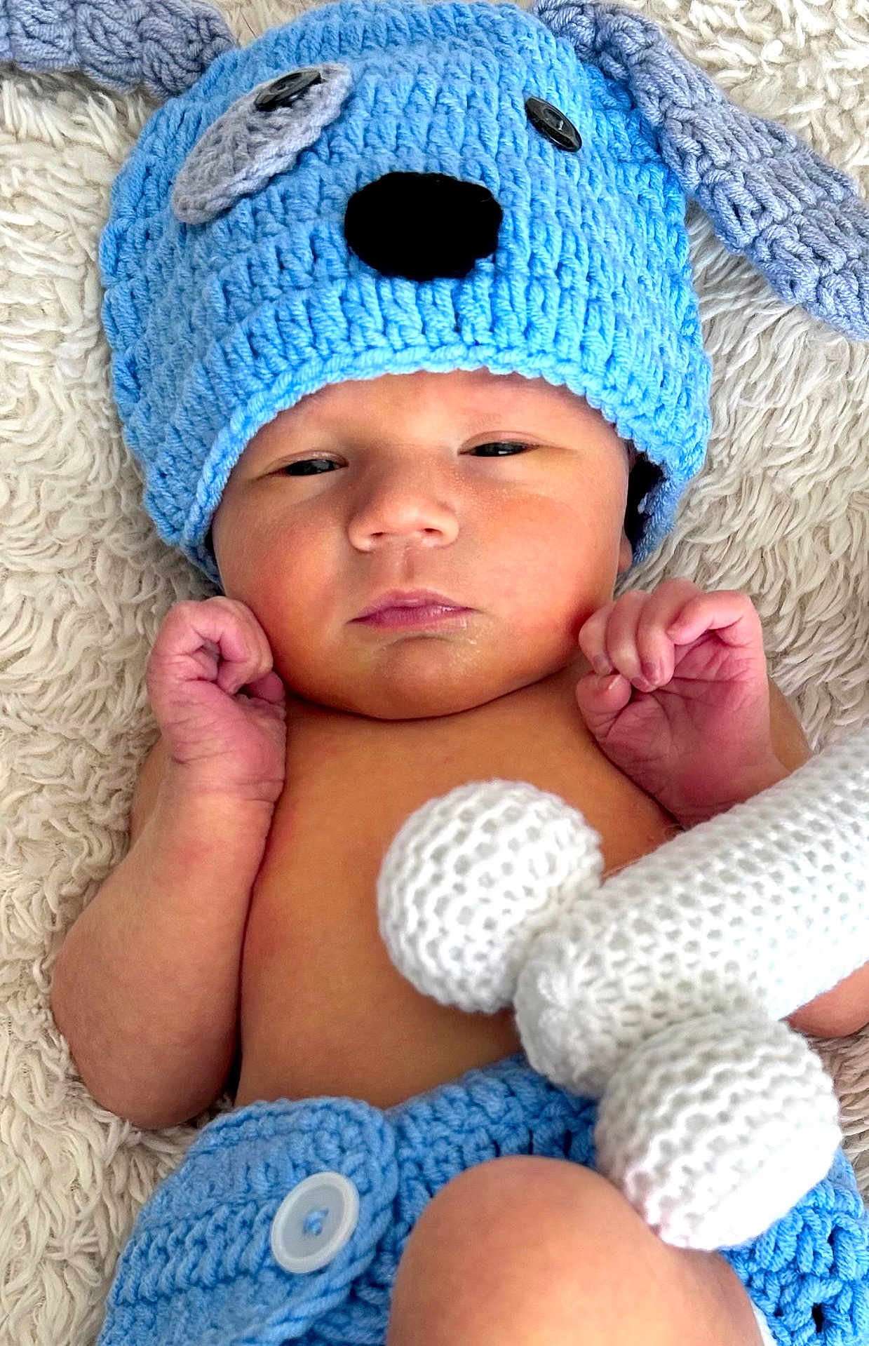 Ronnie joined the competition — help win amazing prizes! baby, infant, crocheted_hat, blue_hat, knitted_toy, blanket, soft_texture, cute, newborn, baby_clothing, hand, face, skin, lying_down, closeup, portrait, relaxed, indoor, baby_boy, button