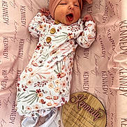 Kennedy joined the competition — help win amazing prizes! newborn, baby, infant, yawning, headband, bow, floral_onesie, pink_blanket, birth_announcement, wooden_plaque, name_kennedy, sleepwear, cute, lying_down, soft, cozy, portrait, indoors, baby_clothes, small_feet