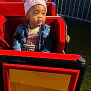 Janae joined the competition — help win amazing prizes! toddler, child, hat, denim_jacket, amusement_ride, red, outdoor, night, park, fence, cute, portrait, smiling, seated, jacket, clothing, play, fun, young, headwear