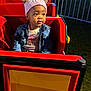 toddler, child, hat, denim_jacket, amusement_ride, red, outdoor, night, park, fence, cute, portrait, smiling, seated, jacket, clothing, play, fun, young, headwear