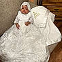 Janae is registered to the contest to win money with this photo: baby, infant, baptism, gown, lace, bonnet, blanket, couch, wood_floor, home_interior, child, portrait, clothing, fabric, furniture, indoors, cute, celebration, religious, toddler