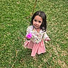 child, girl, grass, outdoor, toy, pink, smile, face, clothing, jacket, skirt, green, nature, standing, person, young, happy, play, casual, daylight