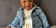 Noah is registered to the contest to win money with this photo: baby, carpet, child, couch, cute, denim_jacket, face, hair, happy, indoor, infant, pants, person, portrait, sign, sitting, smiling, socks, text, wall