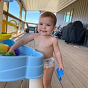 Wrenley is registered to the contest to win money with this photo: toddler, child, smiling, diaper, water_table, toy, outdoor, deck, porch, wooden_floor, grill, furniture, daylight, play, happy, person, baby, summer, fun, casual