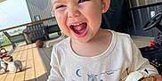 Wrenley is registered to the contest to win money with this photo: child, toddler, laughing, ice_cream_sandwich, outdoor, deck, wooden_floor, toys, shirt, long_sleeve, earrings, smile, happy, person, daylight, play, fun, clothing, background, covered_porch