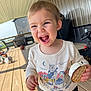child, toddler, laughing, ice_cream_sandwich, outdoor, deck, wooden_floor, toys, shirt, long_sleeve, earrings, smile, happy, person, daylight, play, fun, clothing, background, covered_porch