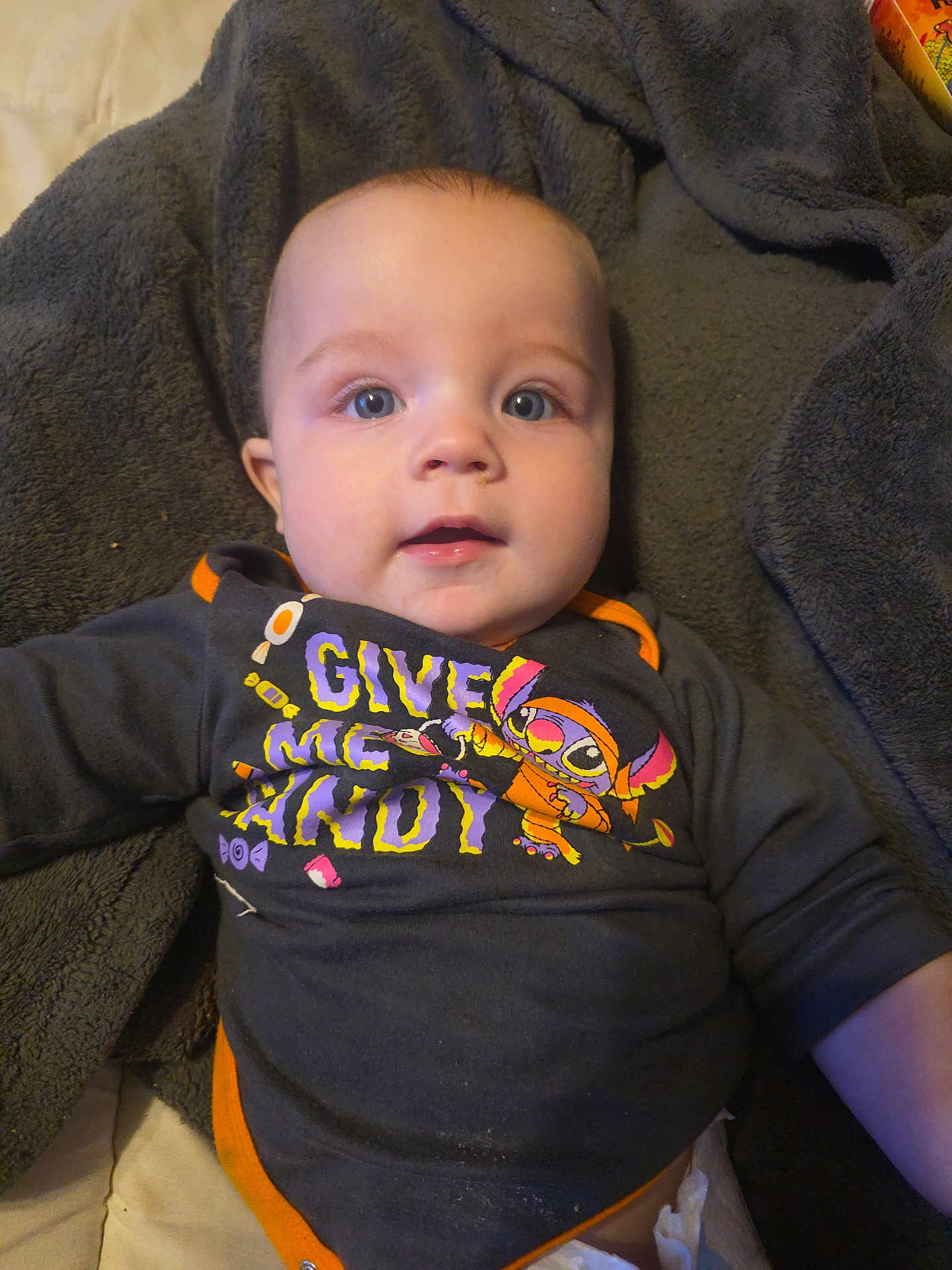 Killian is registered to the contest to win money with this photo: baby, child, infant, face, eyes, blanket, clothing, shirt, cartoon, text, lying_down, indoor, cute, adorable, expression, young, skin, head, portrait, cozy