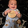 animal_print, baby, blanket, child, cute, elephant, face, giraffe, hands, happy, indoor, infant, lying_down, monkey, onesie, pattern, plaque, portrait, smile, wooden_sign