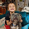 bulldog, chair, child, collar, companion, couch, cozy, dog, family, hugging, indoors, kitchen, leash, living_room, pet, polka_dots, portrait, red_pants, refrigerator, smiling