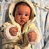 baby, infant, child, portrait, close_up, hooded_robe, blanket, blue_blanket, fluffy, wide_eyed, looking_at_camera, fists, hands, indoor, cozy, lying_down, baby_clothing, soft_texture, warm_lighting, cute