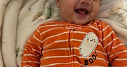 Azael is registered to the contest to win money with this photo: baby, child, infant, smiling, happy, portrait, indoor, blanket, bed, orange_outfit, striped_clothing, ghost_design, boo_text, lying_down, curly_hair, face, eyes, mouth, cozy, family_photo