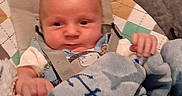 Carson is registered to the contest to win money with this photo: anchor_pattern, baby, baby_seat, blanket, blue, carrying_strap, child, clothing, comfort, cozy, cute, expression, face, head, indoor, infant, person, seat, small_hands, soft_fabric