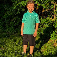 Maher is registered to the contest to win money with this photo: boy, bush, casual_clothing, child, daylight, grass, green_grass, happy, leaves, nature, outdoor, person, polo_shirt, portrait, shoes, shorts, smile, standing, summer, sunlight