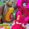 baby, baby_toys, backyard, balloon, bear, birthday_party, blue_eyes, child, face, heart_balloon, hooded_clothing, infant, inflatable_toy, outdoor, pink_outfit, play_mat, portrait, seated, smiling, toys