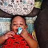 baby, bird, blanket, chewing, child, comfort, couch, crocheted_blanket, cute, face, floral, hand, indoors, infant, pacifier, pattern, pillow, playful, red_onesie, smiling