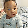 John is registered to the contest to win money with this photo: baby, bed, child, clothing, cozy, curly_hair, cute, dinosaur, expression, face, indoors, onesie, person, portrait, room, sitting, soft_lighting, striped_pants, toddler, young_child