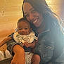 Harrison is registered to the contest to win money with this photo: woman, baby, smile, indoor, denim_jacket, bib, baby_clothes, wooden_wall, happy, holding, infant, person, portrait, casual, child, cute, family, warm_lighting, sneakers, joy