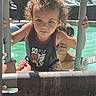 child, pool, water, ladder, curly_hair, swimsuit, summer, outdoor, person, adult, supporting_hand, sunlight, backyard, fence, swimming, playing, happy, fun, family, splash