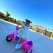 Catriona is registered to the contest to win money with this photo: child, girl, toy_scooter, pink, purple_sunglasses, pigtails, dress, white_sneakers, outdoor, sunny, concrete, play, smile, fun, fence, garden, blue_sky, trees, sidewalk, happy