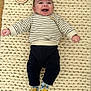 baby, infant, smiling, striped_sweater, dark_pants, colorful_socks, knit_blanket, wooden_plaque, milestone, 3_months, happy, lying_down, cute, child, indoors, floor, portrait, person, young_child, celebration