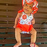 baby, child, bench, hat, floral_pattern, red_clothing, smile, barefoot, bracelet, wood, outdoor, cute, sitting, person, young_child, sunlight, happy, infant, fashion, portrait