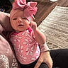 Amara is registered to the contest to win money with this photo: baby, pink, headband, bow, onesie, infant, child, hand, adult, sweatshirt, floor, rug, wooden_floor, pattern, indoor, person, holding, cozy, baby_chair, home
