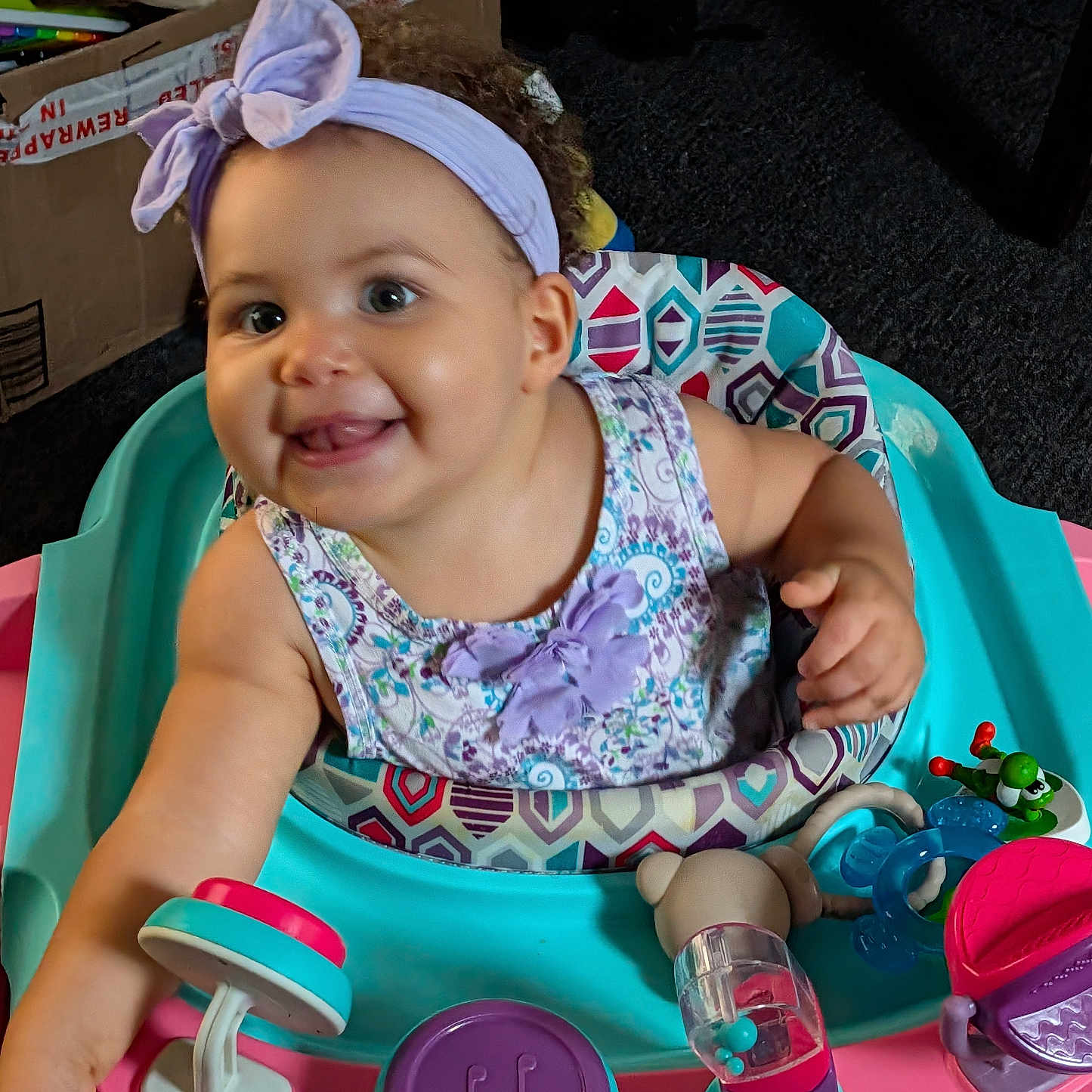 Wynter joined the competition — help win amazing prizes! baby, child, smiling, headband, purple, floral_dress, baby_walker, toys, indoor, carpet, cardboard_box, cheerful, cute, infant, person, playtime, colorful, happy, young_child, seat