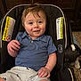 baby, child, smiling, car_seat, blue_shirt, striped_shorts, whale_pattern, toddler, indoor, wooden_dresser, carpet, warning_label, clothing, person, cute, happy, seat, portrait, infant, young_child
