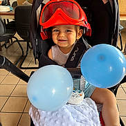 Maëlann participe au concours pour gagner de l'argent avec cette photo : baby, baby_toy, balloon, blanket, chair, child, clothing, cushion, floor, footwear, goggles, happy, headwear, indoor, infant, person, seat, smile, stroller, toy