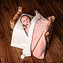 Gabriella is registered to the contest to win money with this photo: baby, blanket, wooden_bed, floor, infant, cozy, wrapped, cute, portrait, child, soft_texture, pink_blanket, white_blanket, wood_grain, newborn, lying_down, face, hand, indoor, warm_lighting