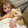 child, girl, puppy, dog, pet, cuddling, indoors, couch, sofa, blanket, cozy, portrait, face, smiling, brown_hair, fluffy, small_dog, home, furniture, companionship