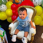 Sebastian joined the competition — help win amazing prizes! toddler, child, chair, balloons, yellow_balloons, red_balloons, white_balloons, paw_prints, casual_clothing, shorts, sneakers, indoor, party_decoration, happy, portrait, baby, furniture, colorful, cute, smiling
