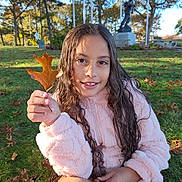 Laura joined the competition — help win amazing prizes! child, girl, leaf, autumn, grass, park, statue, trees, sunlight, outdoor, smile, curly_hair, pink_jacket, fall_leaves, nature, seasonal, casual_clothing, portrait, happy, sitting