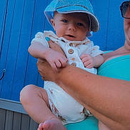 Leland joined the competition — help win amazing prizes! baby, child, blue_cap, white_outfit, adult_arm, turquoise_top, blue_wall, wooden_wall, outdoor, person, infant, holding, cute, portrait, skin, smiling, face, hand, foot, casual_clothing