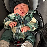 Jaxson is registered to the contest to win money with this photo: baby, infant, car_seat, clothing, beanie, jacket, plaid, buttons, face, hand, footwear, socks, expression, winking, child, seatbelt, casual, cute, indoor, portrait