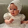 Ellie is registered to the contest to win money with this photo: baby, infant, child, white_dress, lace_bonnet, puffy_sleeves, cute, portrait, smiling, sitting, couch, indoor, soft_lighting, closeup, happy, face, hands, young, elegant, adorable