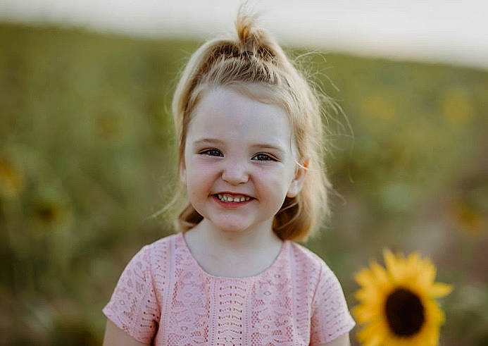Paisley is registered to the contest to win money with this photo: asterales, baby_toddler_clothing, blond, brown_hair, child, child_model, daisy_family, ear, eyelash, facial_expression, hairstyle, happy, iris, joy, mouth, organ, person, petal, summer, sunflower
