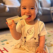 Anastasia is registered to the contest to win money with this photo: toddler, child, baby, sitting, comb, headband, bow, hair, smiling, barefoot, shoe, playmat, indoor, cute, happy, clothing, person, face, hand, living_room