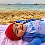 baby, beach, beanie, blanket, boat, child, clothing, eyes, happy, hat, infant, ocean, portrait, red_hat, relaxing, sand, sea, shore, smile, towel