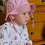 blue_eyes, child, crayon, cute, face, focused, furniture, hat, holding_object, indoor, patterned_clothing, person, pink_hat, portrait, sitting, skin, toddler, white_clothing, wooden_dresser, young_child