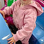Eliza joined the competition — help win amazing prizes! toddler, child, hoodie, pink_clothing, play_area, arcade_ride, colorful, indoor, toy, hand, face, eyes, expression, curious, playful, seat, footwear, sock, young_child, person