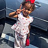 toddler, child, smiling, peace_sign, red_bow, strawberry_pattern, outdoor, parking_lot, shoes, sandal, purse, sunlight, shadow, clothing, person, cute, happy, curly_hair, gesture, casual