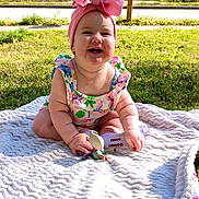 Hazel is registered to the contest to win money with this photo: baby, child, smiling, outdoor, grass, blanket, headband, pink_bow, toy, sunlight, happy, cute, infant, sitting, colorful_clothing, nature, portrait, daylight, playful, cheerful