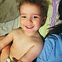 toddler, child, smiling, face, bare_chest, diaper, blanket, pattern, hair, joyful, person, indoors, lying_down, closeup, happy, skin, head, shoulder, blue_shirt, candid